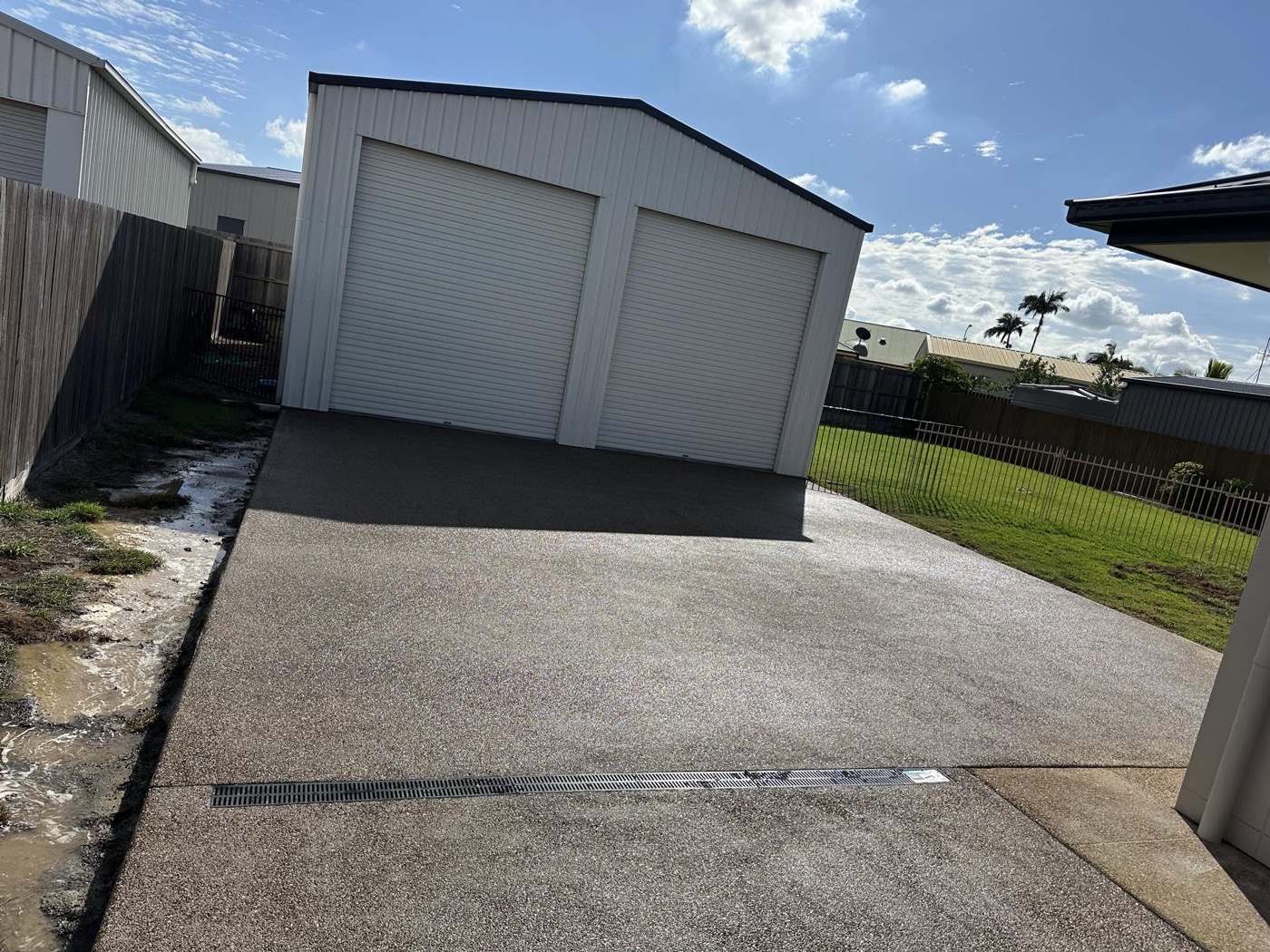 A wide concrete driveway leading to a colourbond shed