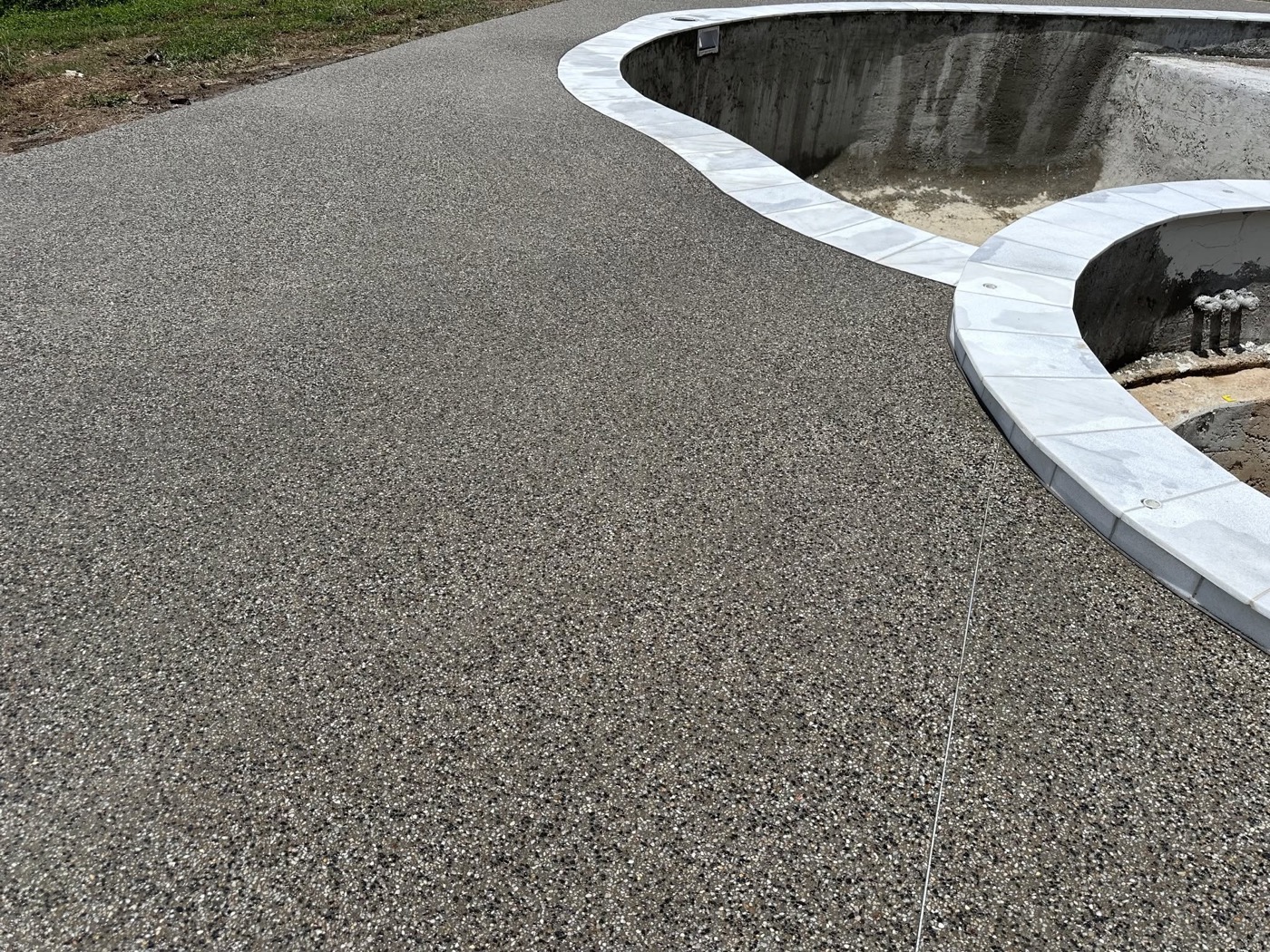 An exposed aggregate apron curving around the edge of a pool shell