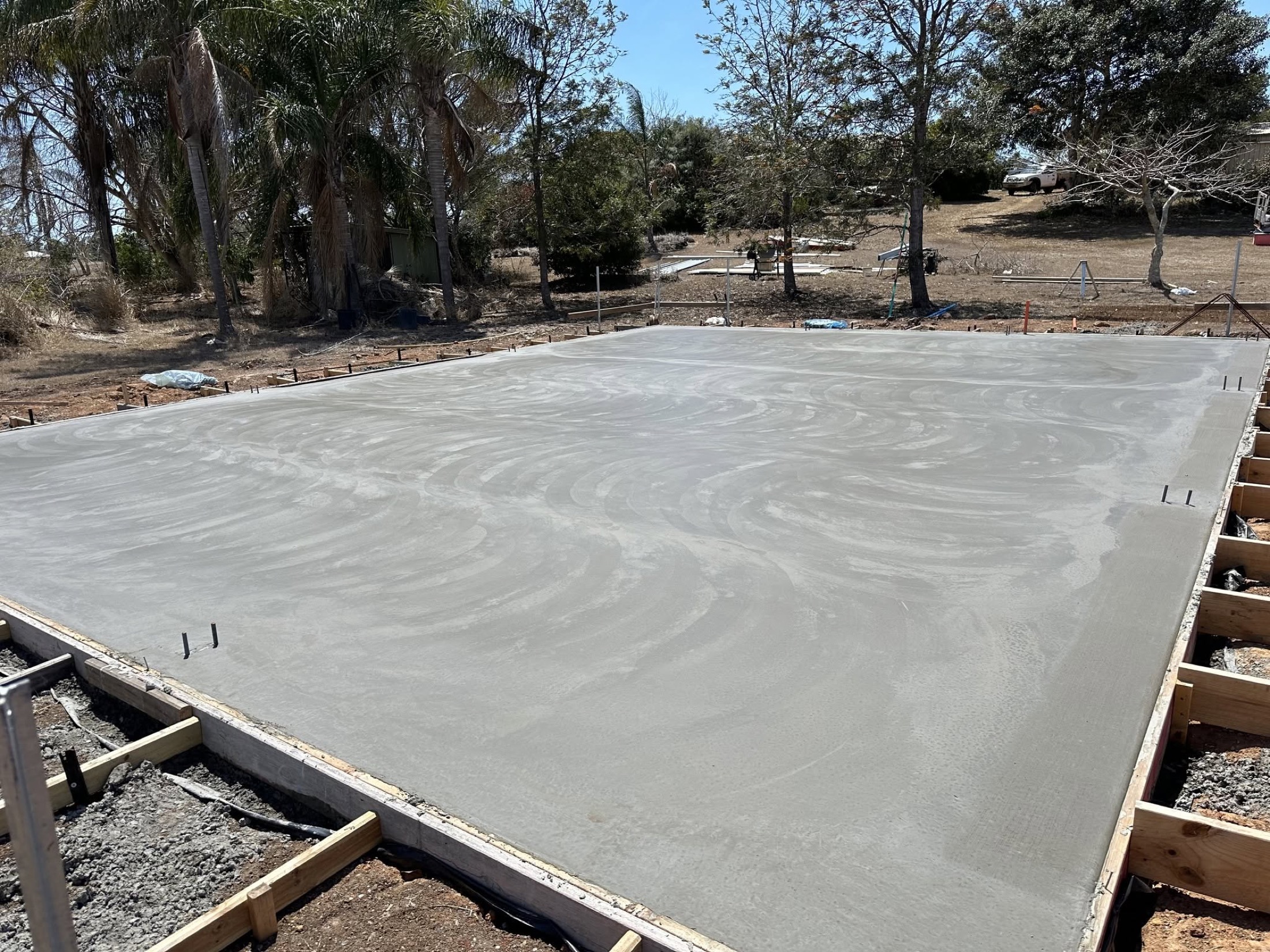 A large freshly floated concrete slab with palms and gum trees at the boundary