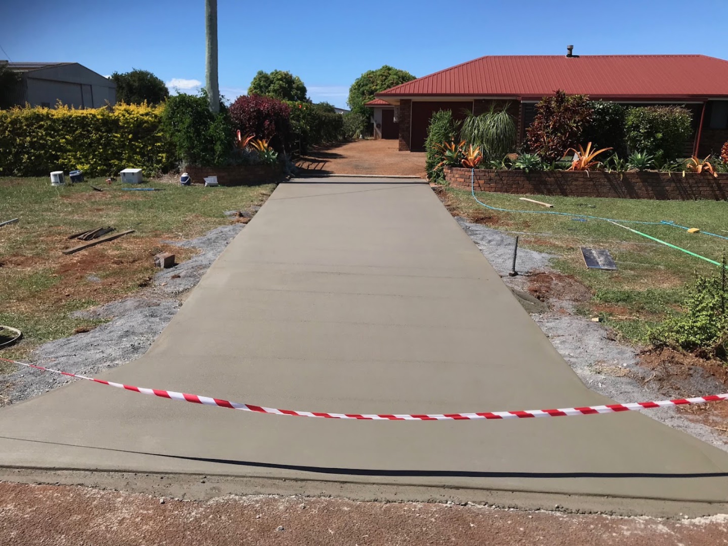 A long concrete path leading up to a red-roofed home through a garden