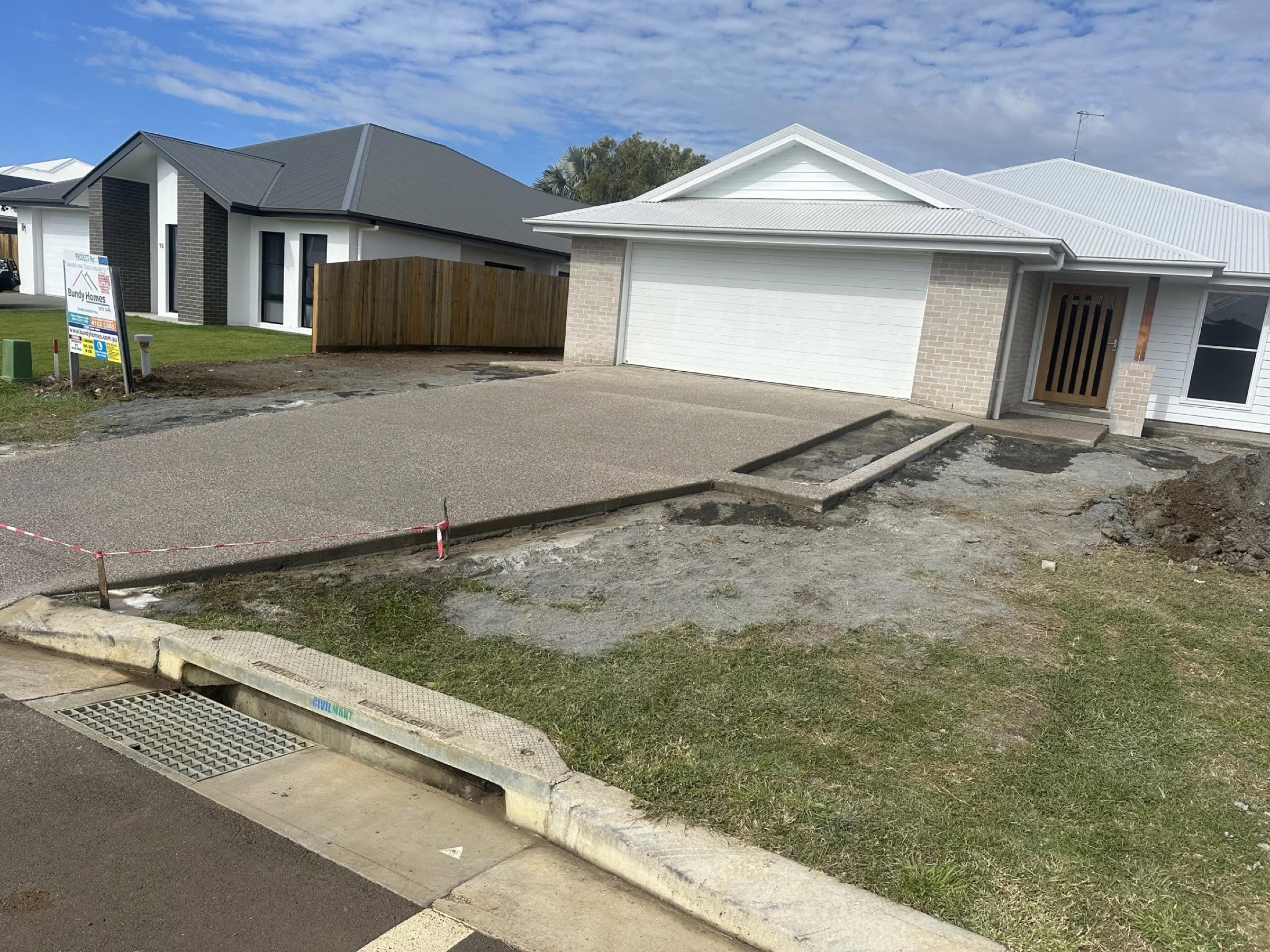 An exposed aggregate driveway running up to a new brick home under a bright Queensland sky