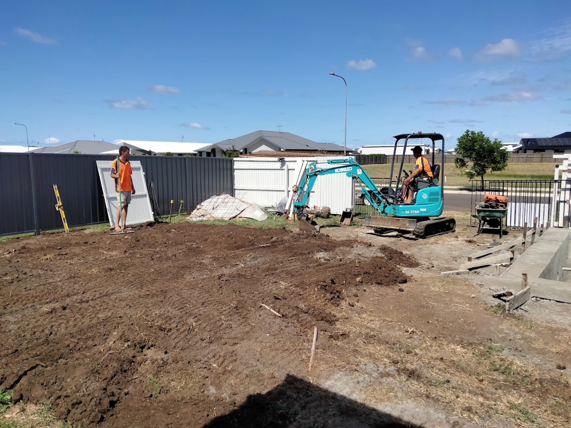 Two workers in high-visibility shirts preparing a site with a mini excavator beside a formed slab edge