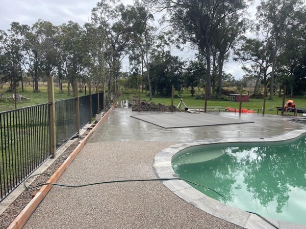 A swimming pool with an exposed aggregate surround and gum trees behind it