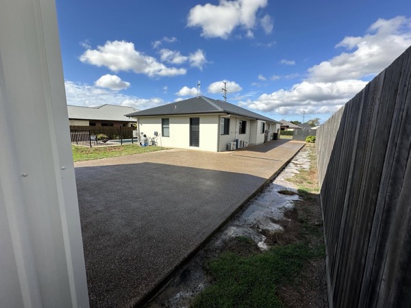 An exposed aggregate driveway between a house and a timber fence