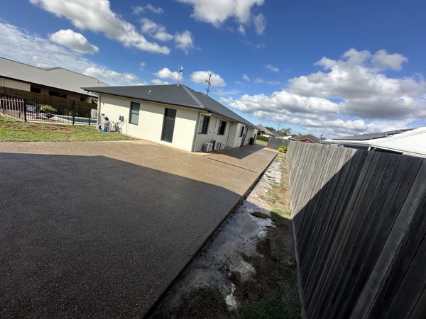 A curved exposed aggregate driveway beside a rendered home