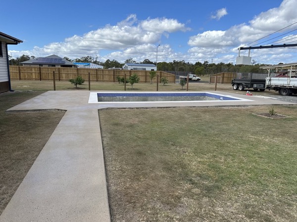A finished swimming pool with a concrete apron and lawn
