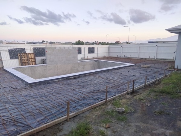 Reinforcing mesh laid over membrane inside formwork beside a pool shell