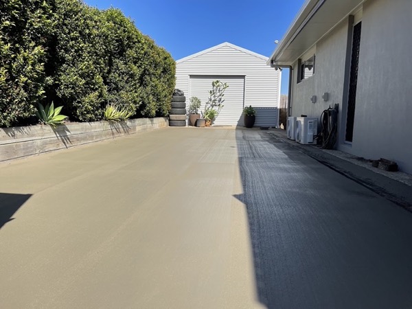 A concrete driveway running between a house and a shed