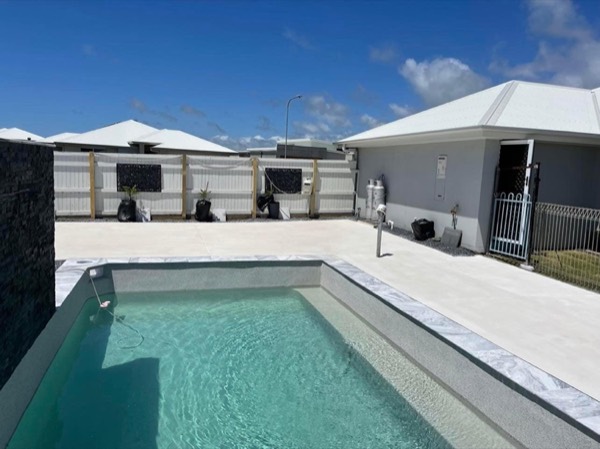 A rectangular pool with a concrete surround beside a house