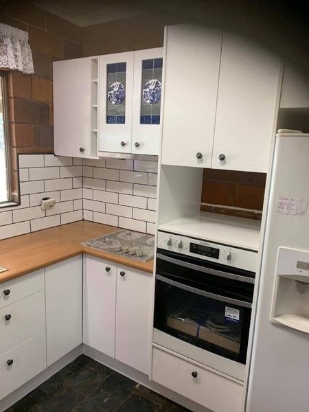 Kitchen cabinetry with a white subway splashback and a wall oven