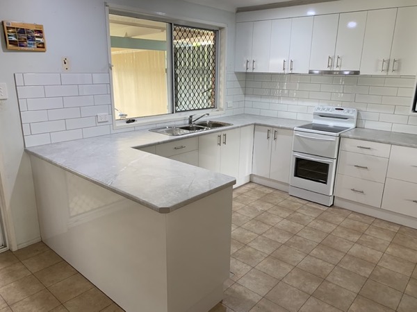 A white kitchen with a peninsula bench, sink and freestanding oven